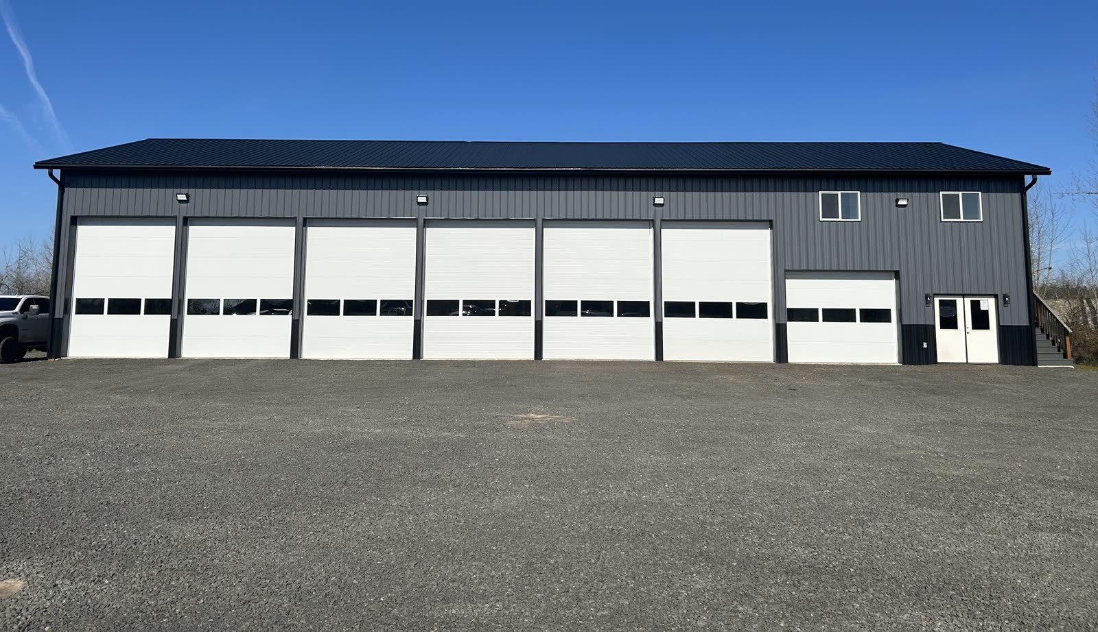 The KS Automotive Repair workshop, a long dark steel building with seven white bay doors on a fresh gravel lot under a clear sky.